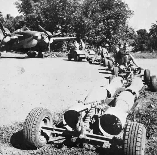 (1B) Armourers ride a bomb train loaded with 250-lb GP bombs to a Bristol Blenheim Mark V of No. 34 Sqdn, parked in dispersal o