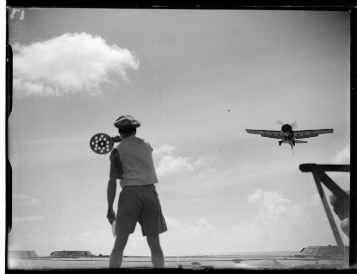 The flight deck officer guiding a Grumman Martlet of 888 Squadron, Fleet Air Arm into land with his bats on board HMS FORMIDABL